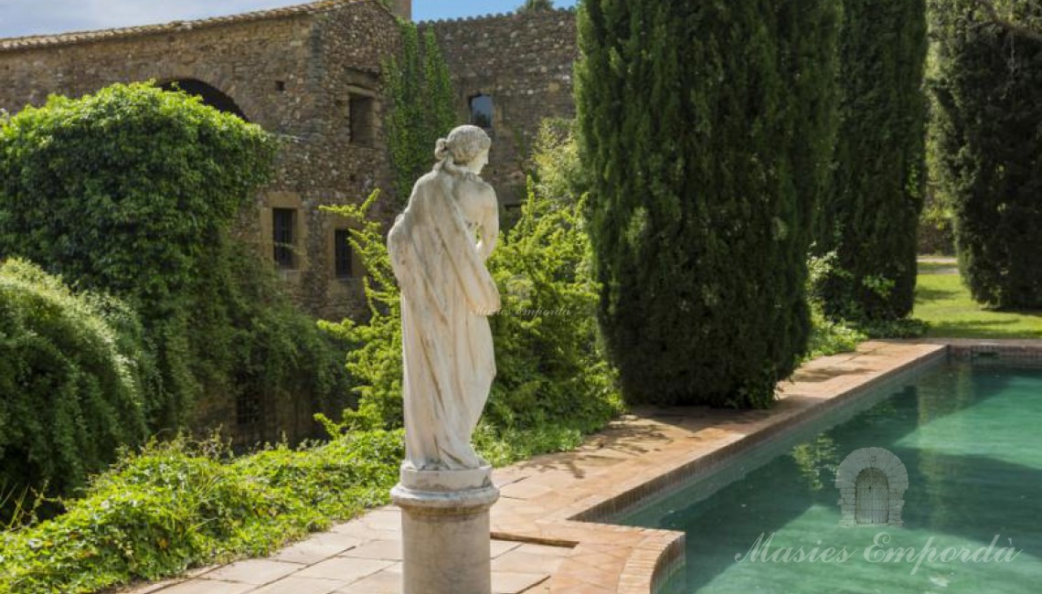  Vista de la piscina rodeada de cipreses con una preciosa estatua estilo romano y como fondo la masía  