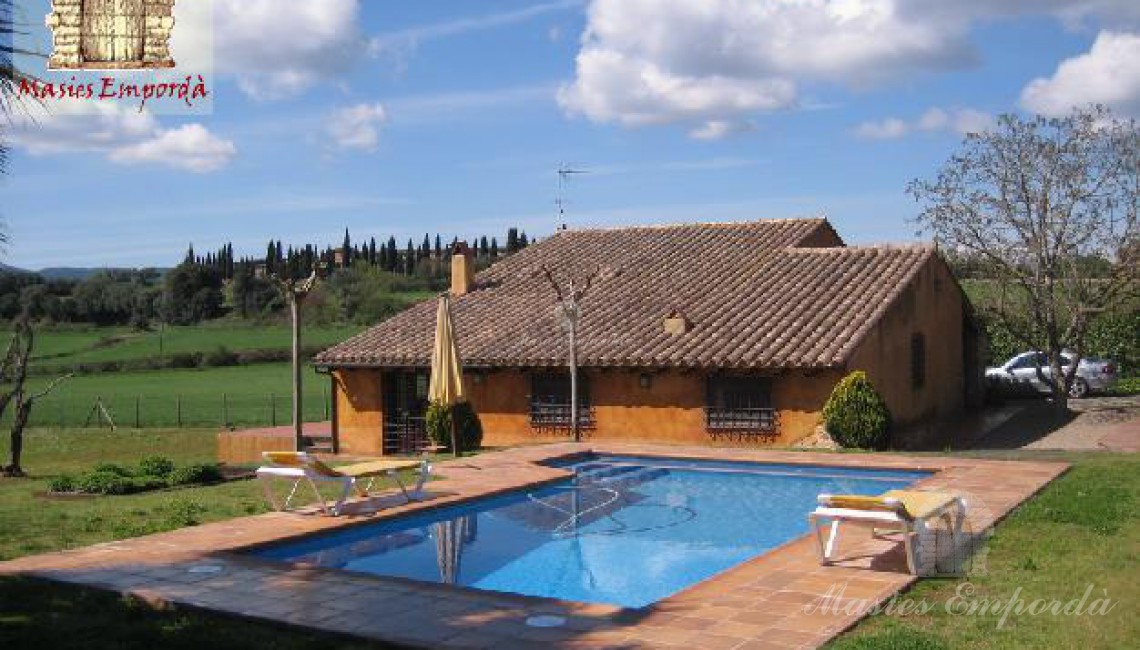 Vista de la piscina con la casa al fondo y todo el conjunto rodeado de jardín 