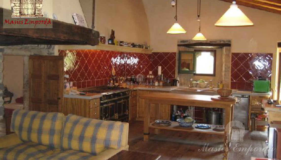 Cocina de la masía con chimenea abierta y salón 