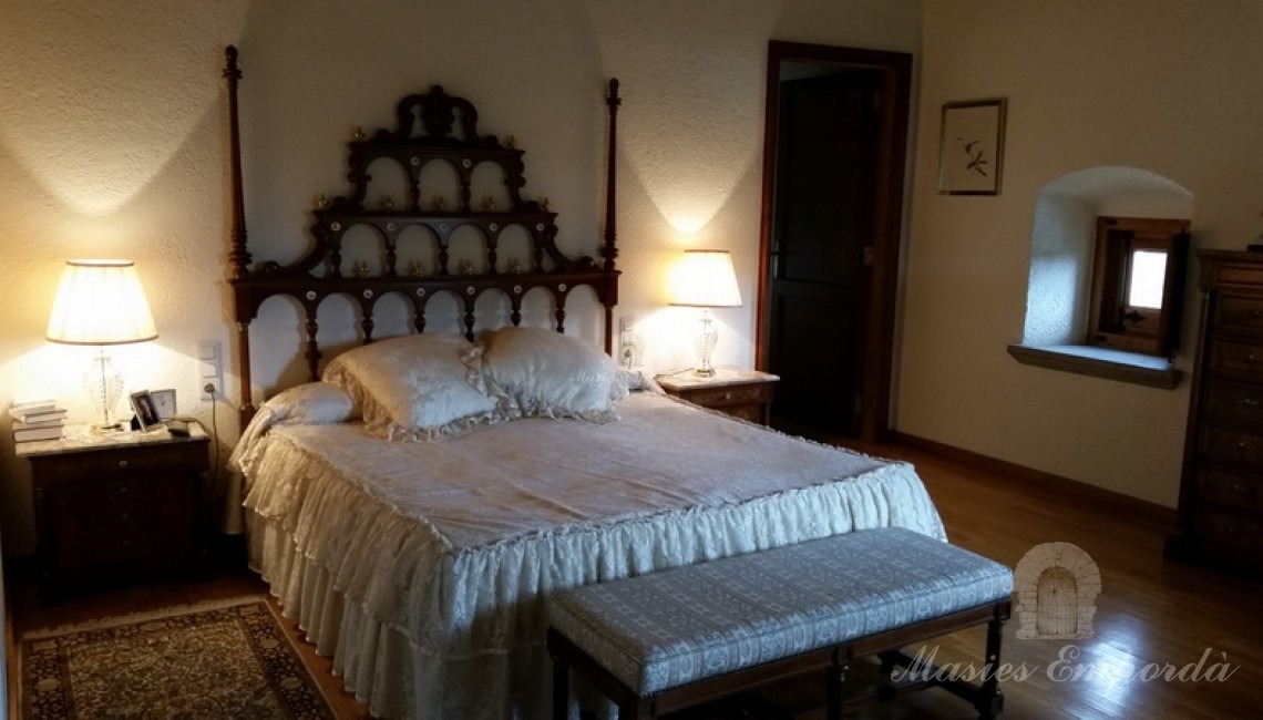 Unas de las suites de la masía con cama doble y cabezal de cama en madera labrada  