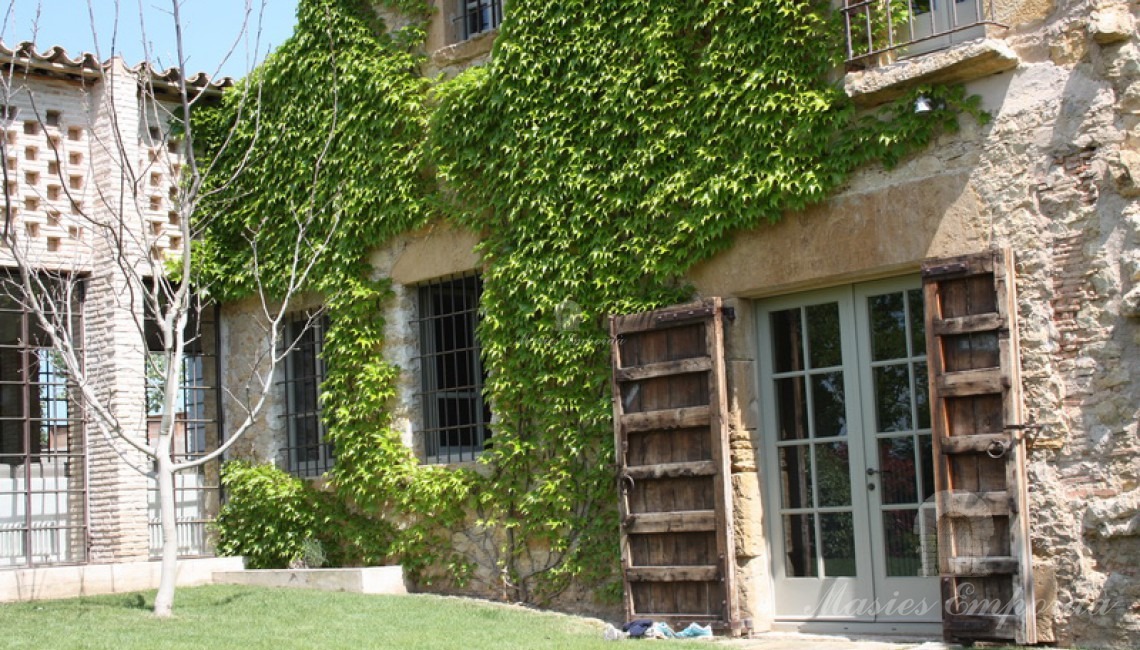 Detalle de la fachada de piedra de la casa con los portones de madera abiertos  con el pabellón de verano en un lateral de la imagen 