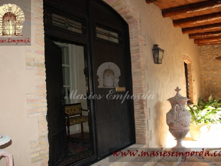 Gran puerta principal de madera y contra puerta interior también de madera y acristalada con el porche corrido en fachada con vigas de madera  