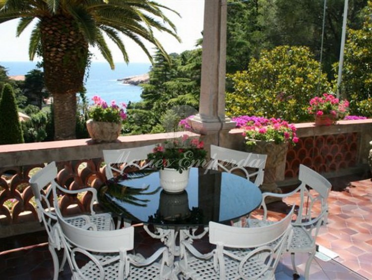 Detalle de la terraza con una mesas de té con forndo del jardin y el mar